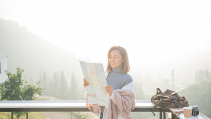 Wall Mural - Girl tourist in mountain read the map and looking mountain view at countryside homestay in the morning sunrise with copy space. journey, trip and relaxing concept. coats blankets in winter.