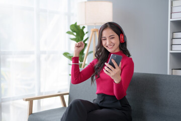 Happy young Asian woman raising hands with victory smiling happily with smart phone at home. Success, win, victory, triumph, congratulation, concept.