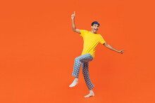 Full body side view happy young man wear pyjamas jam sleep eye mask rest relax at home look camera raise up hands leg isolated on plain orange background studio portrait. Good mood night nap concept.