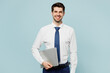 © ViDi Studio - Young fun smiling employee IT business man corporate lawyer wear classic formal shirt tie work in office hold closed laptop pc computer isolated on plain pastel light blue background studio portrait.