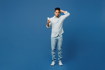 Wall Mural - Full body sad young man of African American ethnicity he wear casual clothes shirt hold head use mobile cell phone isolated on plain dark royal navy blue background studio portrait. Lifestyle concept.