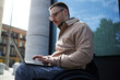 © AnnaStills - Young man with disability sitting in wheelchair with laptop and concentrating on his online work, he working outdoors