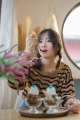 Asian girl sitting in cafe near window smiling in cafe vintage color tone enjoy eating ice-cream.