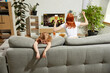 © master1305 - Young excited woman sitting on couch at home and emotionally watching football match on tv while little girl, child feeling bored. Concept of hobby, entertainment, lifestyle, sport, leisure, emotions