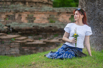 Wall Mural - Pretty Asian tourists woman wearing beautiful hand-woven clothes dyed with indigo and mud-fermented natural colors modern Thai traditional dress costumes are popular in ancient temple Thailand.