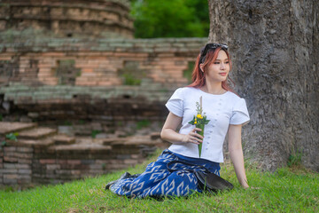 Wall Mural - Pretty Asian tourists woman wearing beautiful hand-woven clothes dyed with indigo and mud-fermented natural colors modern Thai traditional dress costumes are popular in ancient temple Thailand.