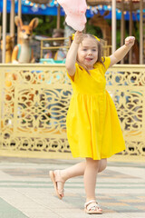 Wall Mural - Little girl with cotton candy in an amusement park. The concept of summer holidays and school holidays