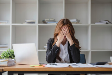 A stressed and serious young Asian businesswoman focuses on working on her business financial reports at her desk in the office.