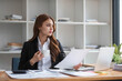 © wichayada - A beautiful young Asian businesswoman in a formal business suit is using her laptop and working on marketing reports at her desk in the office.