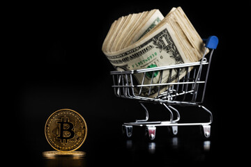 Coin with bitcoin cryptocurrency symbol and shopping trolley with 1 american dollar banknotes on black background