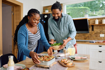 Wall Mural - Happy African American couple bringing food at dining table.