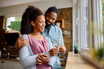 Wall Mural - Happy black couple toasting while drinking wine at home.