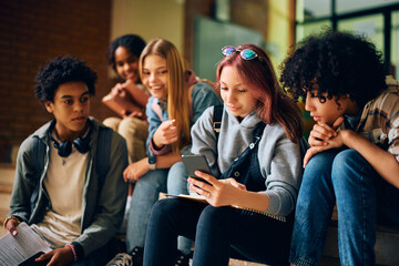 Wall Mural - Teenage girl and her friends using mobile phone in hallway at high school.