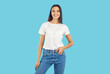 Studio shot of a young female model posing in casual clothes. Happy beautiful woman wearing a white mockup T shirt and comfortable blue jeans standing isolated on a blue background. Fashion concept