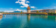 Picturesque panorama photo of the famous diagonal wooden covered footbridge, the Kapellbrücke (Chapel Bridge), with the Water Tower over the river Reuss in Lucerne and mountains in the background. 