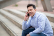 © mimagephotos - Confident latin man sitting outdoors on steps talking on mobile phone
