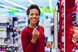 © bnenin - Portrait of a smiling African woman picking a lip pencil in a  beauty section.