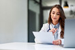 © bnenin - A smiling female doctor reading results on paper while sitting at the office.