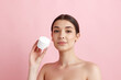 © master1305 - Portrait of young beautiful woman posing with face moisturizing cream against pink studio background. Organic cosmetics. Concept of natural female beauty, body and skincare, cosmetology, health, ad