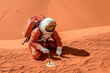 an astronaut kneeling in the sand with his hands on his knees, looking down at something he has just done