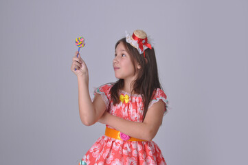 menina comendo pirulito colorido, criança com vestido tradicional de festa junina, festa de são joão