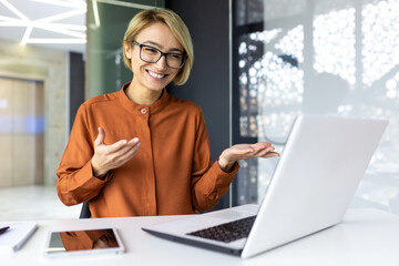 Happy businesswoman working in modern office using laptop for video call and online meeting with fellow employees, woman smiling and having fun giving a presentation.