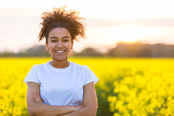 Wall Mural - Beautiful mixed race African American girl teenager female young woman happy smiling with perfect teeth at the end of a path in a field of yellow flowers