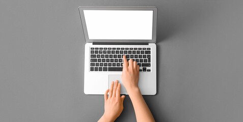 Hands of woman using laptop on grey background, top view