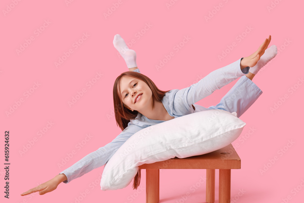 Little girl with pillow lying on bench against pink background
