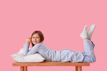 Wall Mural - Little girl with pillow lying on bench against pink background