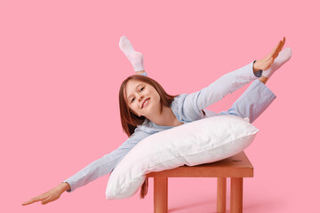 Wall Mural - Little girl with pillow lying on bench against pink background