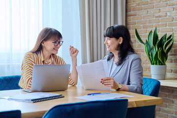 Two mature business women working in office, with papers, laptop