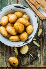 Sticker - Peeled potatoes. Peeling a potato with peeler in a kitchen on a wooden rustic table. Top view