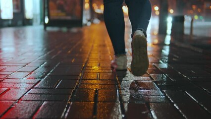 Wall Mural - rear view of the legs of a girl walking in front of the camera on a wet road