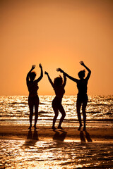 Wall Mural - Three beautiful young women in bikinis dancing on a beach at sunset all in silhouette