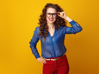 Wall Mural - Portrait of smiling trendy woman with long wavy brunette hair in glasses isolated on yellow background