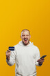 © Davidovici - Vertical photo of excited man holding phone and credit card while shouting, standing isolated over yellow background. Empty space, mobile payment.