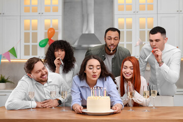 Happy friends with tasty cake celebrating birthday in kitchen