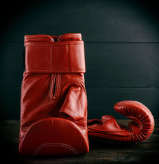 pair of red leather gloves for boxing on a brown wooden table, black background