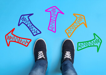 Wall Mural - Choosing future profession. Teenager standing in front of drawn signs on light blue background, top view. Arrows pointing in different directions symbolizing diversity of opportunities