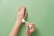 Female hand model using a silicone brush to apply cream or lotion on her hand. Green pastel background. Cosmetic skin care product texture