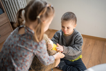 Wall Mural - Boy plays with his younger sister on the bed in home bedroom. Down syndrome and ASD