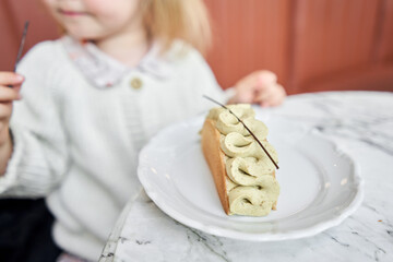 selective focus a child is sitting at a table in a cafe and trying a delicious dessert. a cute little girl eats dessert with pistachio cream in a cafe. Children's cafe.