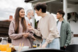 © LIGHTFIELD STUDIOS - happy middle aged mother holding cherry tomato and talking with teenage daughter, family grill party, father and son on blurred background, happy parents day concept, summer