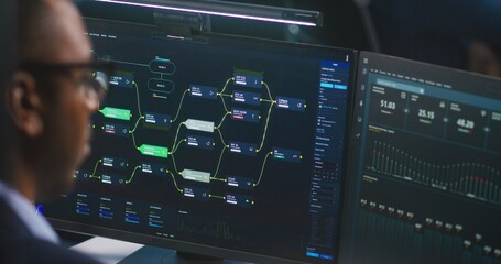 African American software engineer looks at computer screen with displayed big data server and blockchain network, monitors real-time analysis charts in monitoring office. Concept of cyber security.