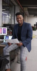 Wall Mural - vertical video of african american male creative reading document at casual office, in slow motion