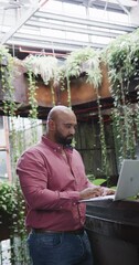 Wall Mural - vertical video of happy biracial male creative using laptop at casual office, in slow motion