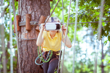 The girl plays a virtual game, she goes in for sports virtually. Virtual reality glasses help in sports. Virtual glasses are immersed in a children's forest rope adventure park.