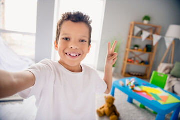 Portrait of positive boy recording video make v sign call parent feedback from montessori primary school indoors