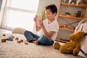 Sticker - Photo of positive boy sit floor carpet in preschool interior use gadget choose new toy from website buying on birthday